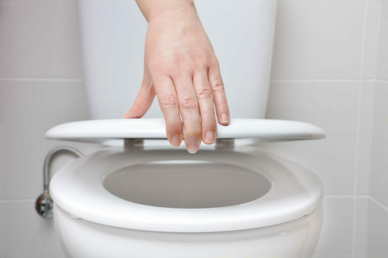 Hand of a woman closing the lid of a toilet