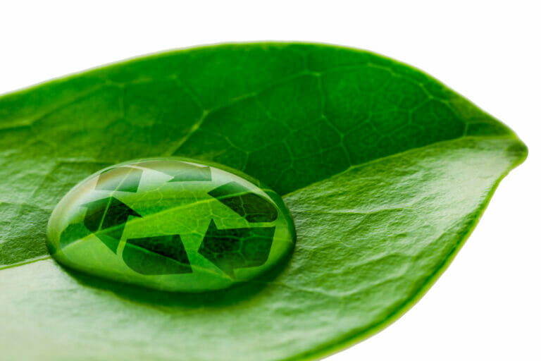 A clear water droplet rests on a green plant leaf, and within it, there's a small recycling symbol, emphasizing the concept of environmental sustainability.