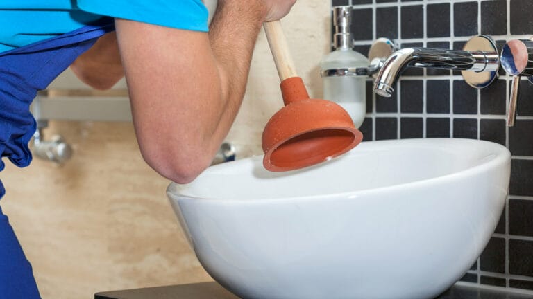 Professional plumber using a plunger on a white bathroom sink, demonstrating a method to clear a clogged drain.