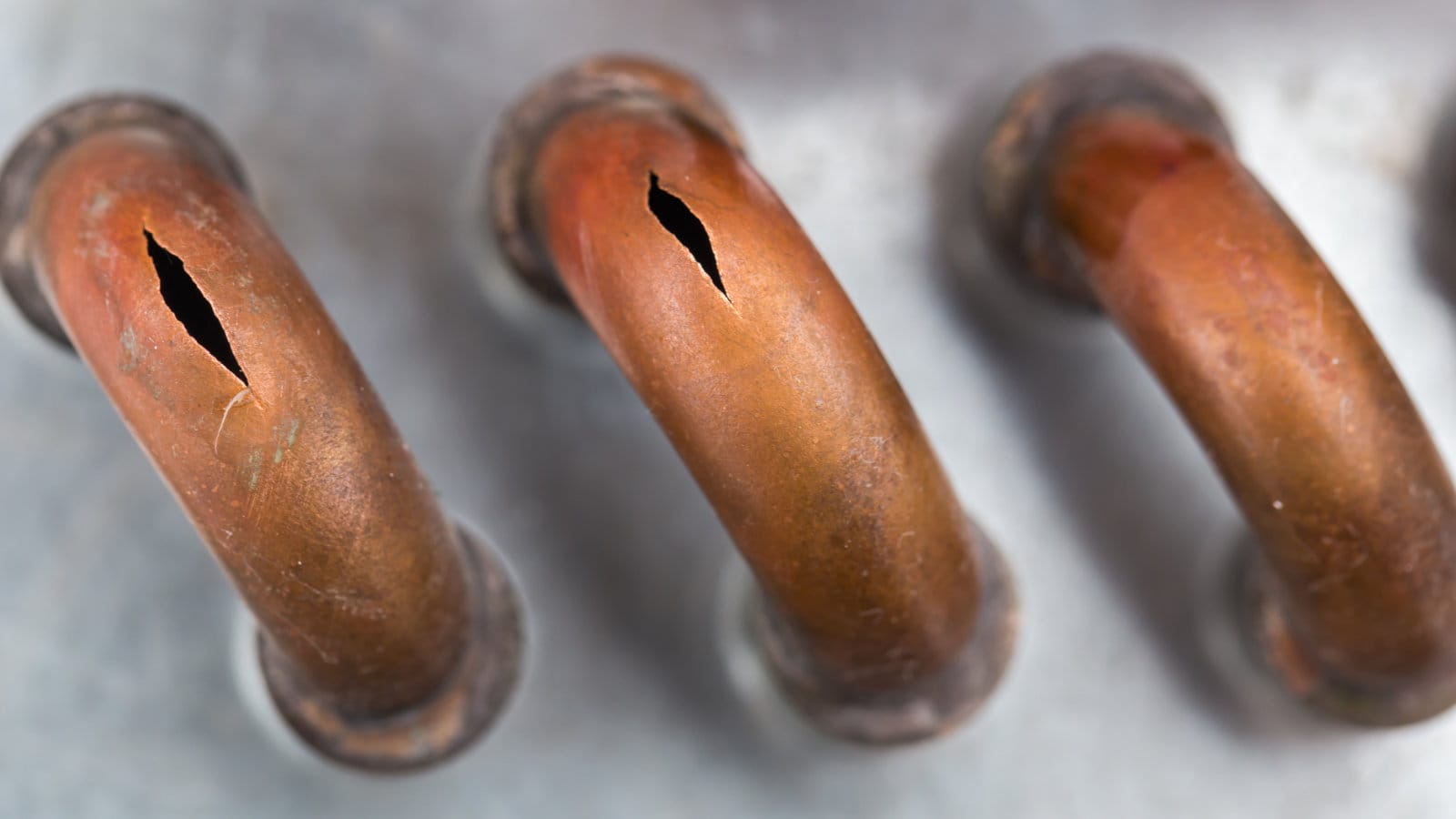 Close-up of damaged and corroded copper pipes with visible cracks, indicative of potential gas leaks in a home.