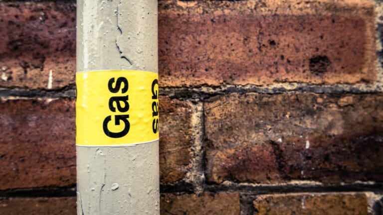 Close-up of a residential grey gas pipe with a prominent yellow 'gas' sticker, installed against a textured red brick wall, highlighting home gas safety and infrastructure.