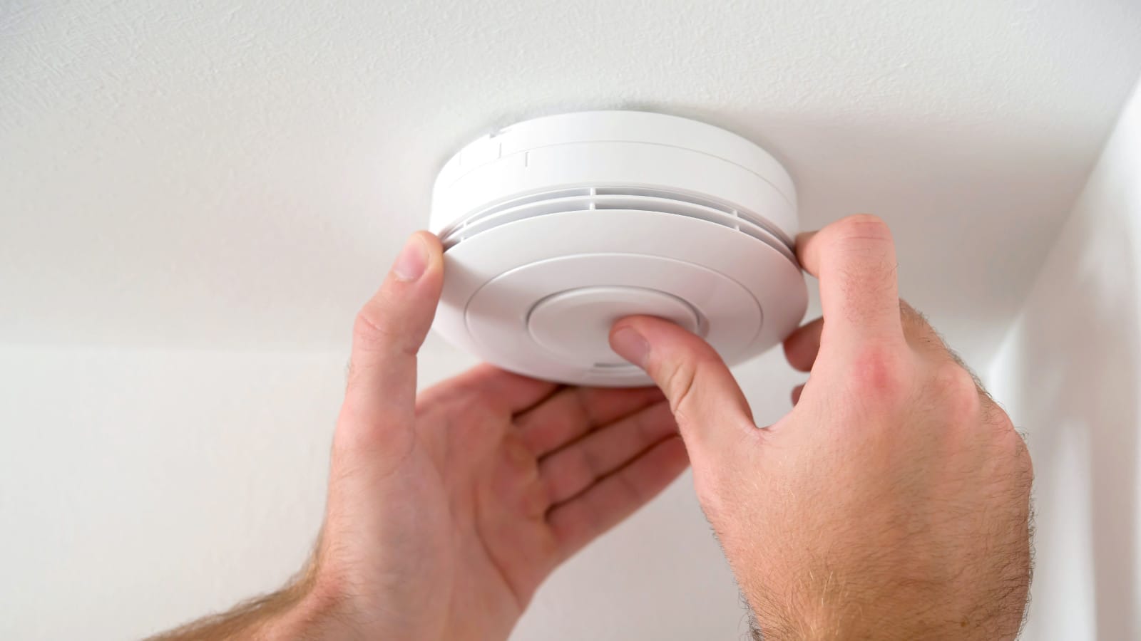 A person's hands installing a white carbon monoxide detector on a ceiling, emphasizing proper placement in a Rockwall, TX home for safety against gas leaks.