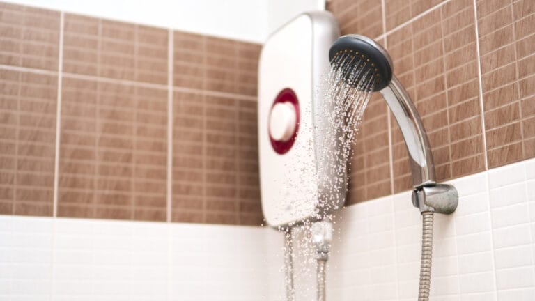 Electric shower unit with water flowing from the showerhead against a backdrop of ceramic tiles, depicting routine maintenance for efficient water heating.