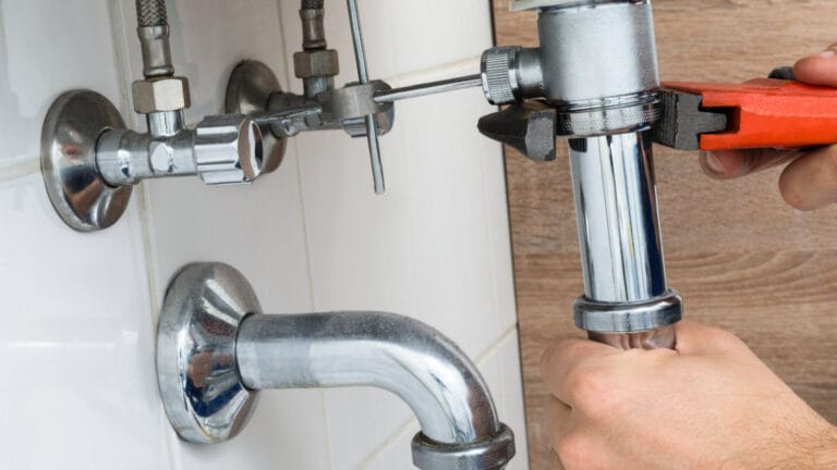 A plumber's hands using an adjustable wrench to tighten a sink's U-trap, illustrating routine home plumbing maintenance