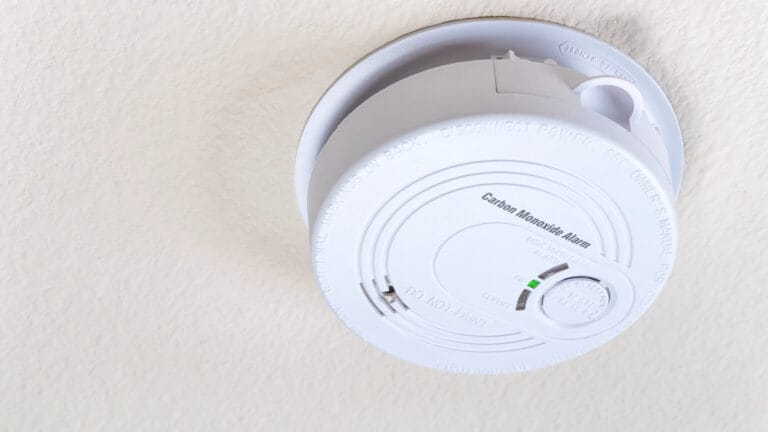 Carbon monoxide detector mounted on a ceiling with a green indicator light on, signifying operational status, in a residential setting, illustrating the importance of functioning alarms for home safety.