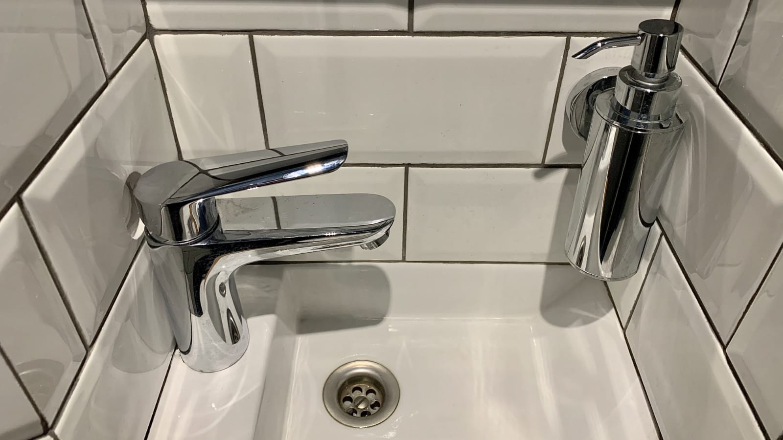 A modern chrome faucet and soap dispenser set against white subway tile over a bathroom sink, reflecting potential areas of concern for new homeowners assessing plumbing conditions.