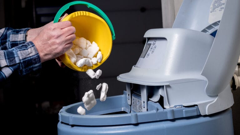 Person pouring salt pellets into a water softener tank as part of routine maintenance, illustrating the process of water softening which replaces minerals like calcium and magnesium with sodium.