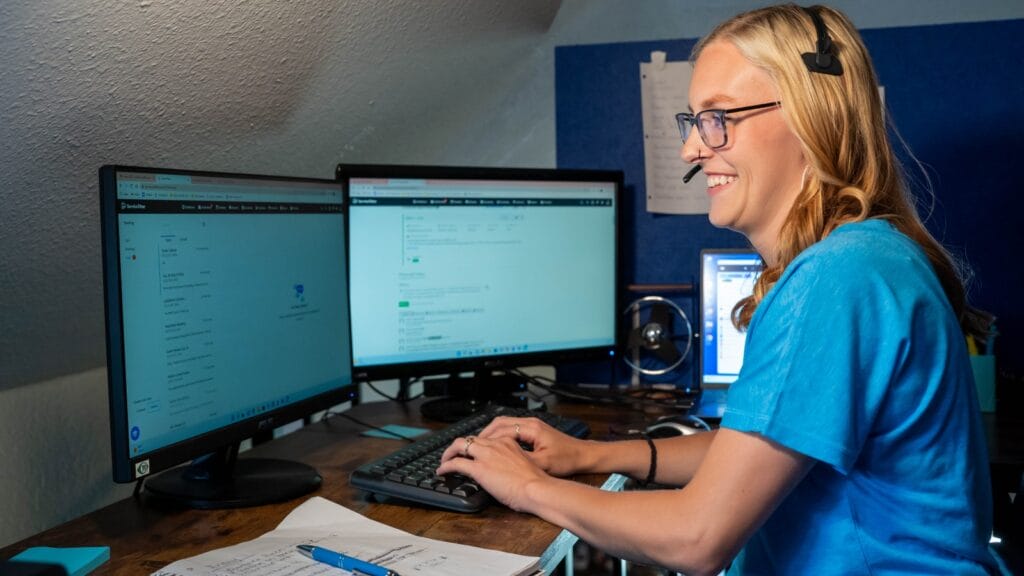 A customer service representative at a plumbing company using advanced software on dual monitors to schedule and manage plumbing services.