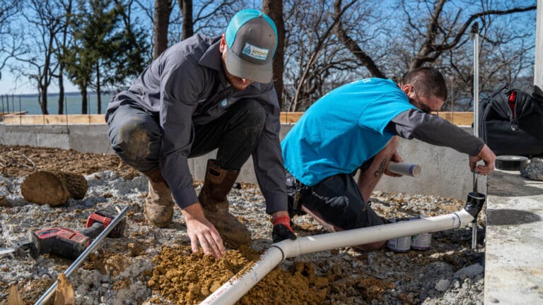 Two plumbers working outdoors on a sewer line installation, illustrating professional help for fixing clogged sewer lines.