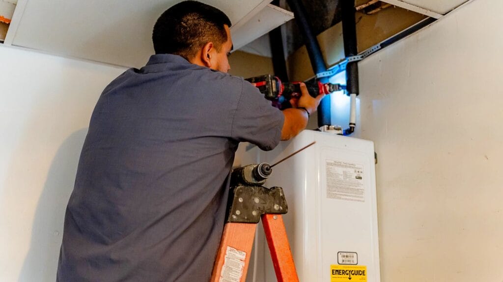 Plumber installing a tankless water heater indoors, using a power drill to secure components for safe and efficient operation